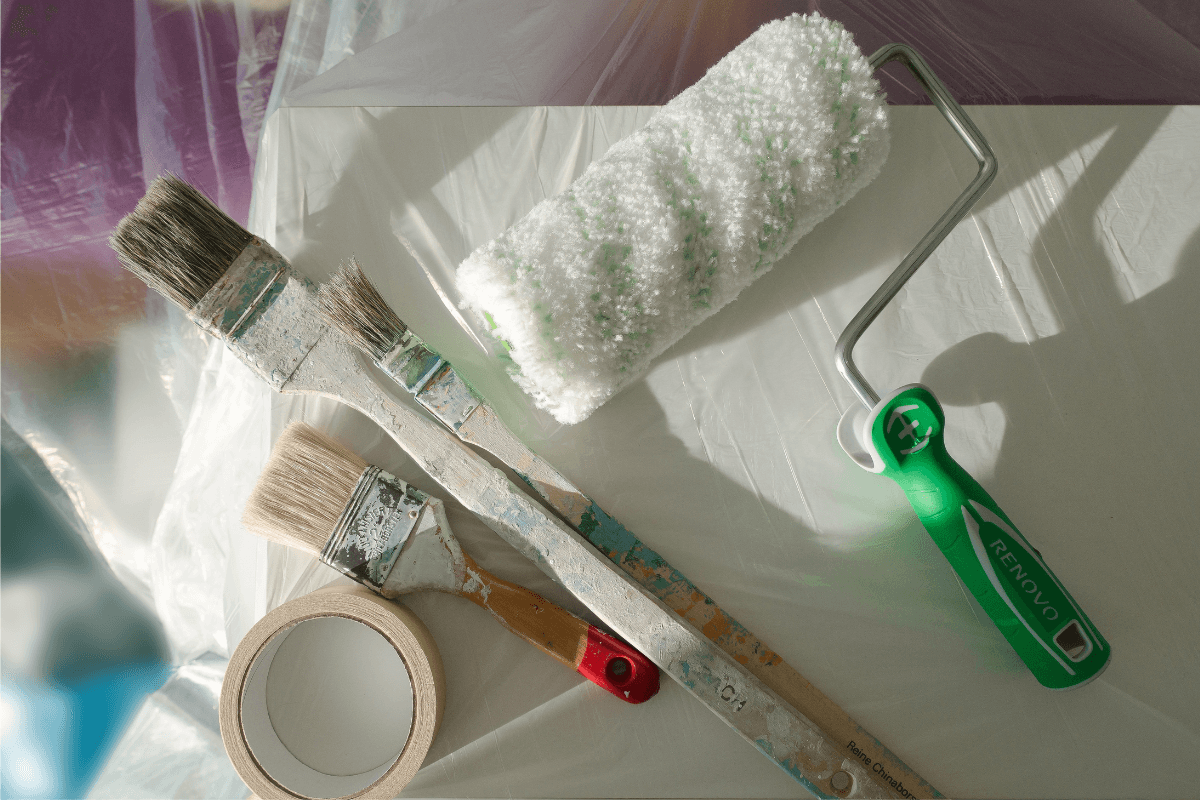 Brochas profesionales y rodillo de pintor sobre superficie protegida con plástico